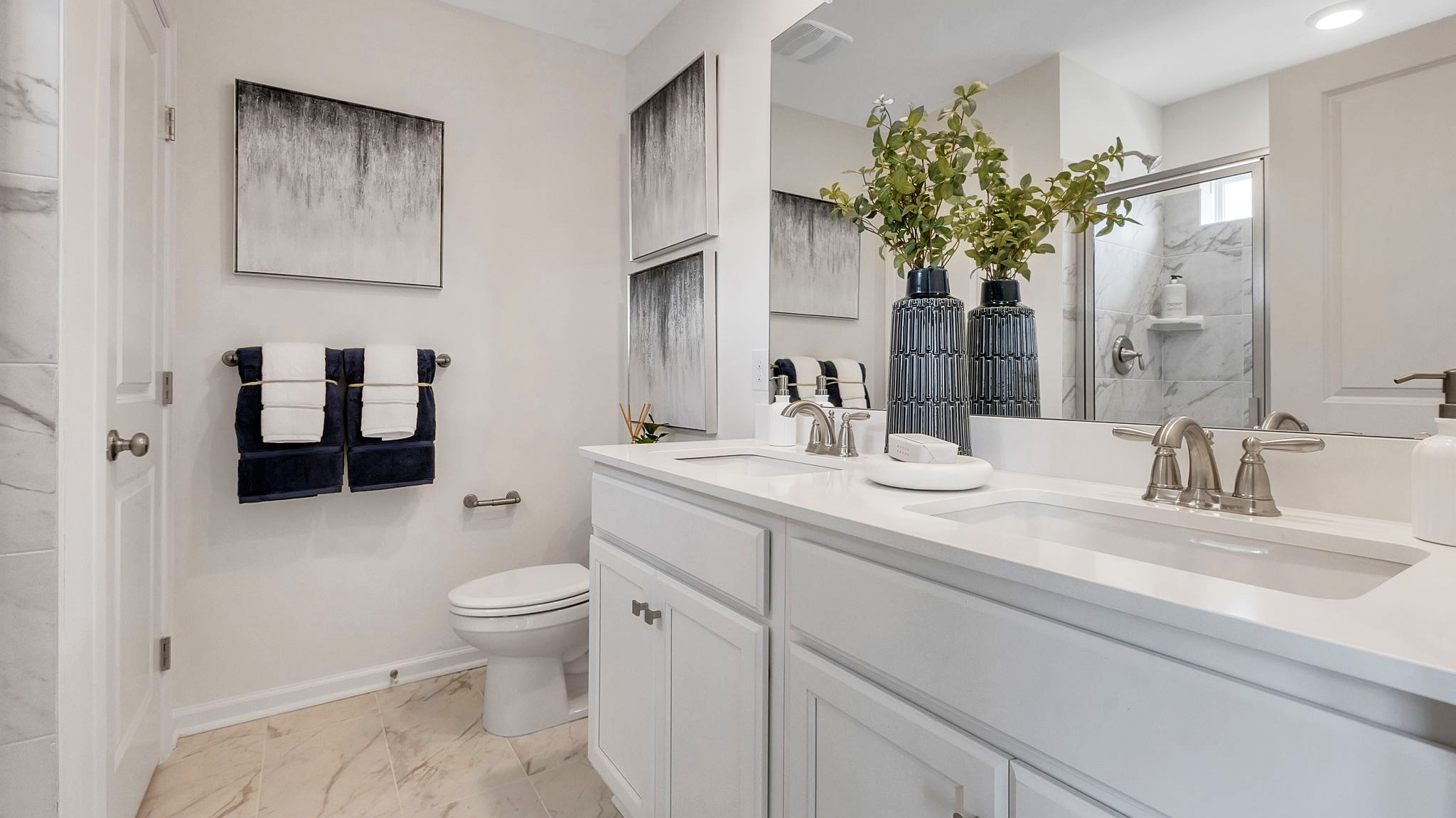 Primary bathroom with double sink white vanity with glass door shower and linen closet.
