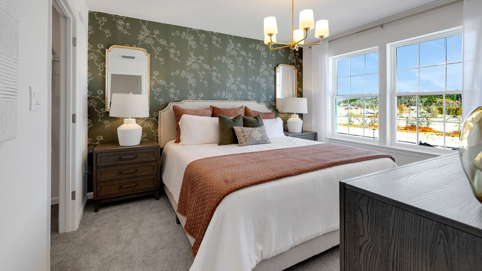 Primary bedroom with a king size bed and end tables and two large windows.