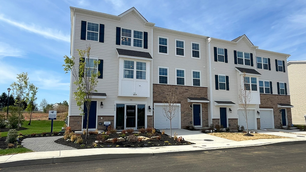 Exterior front image of the model townhome with cream horizontal panel siding and stone kneewall with white single car garage.