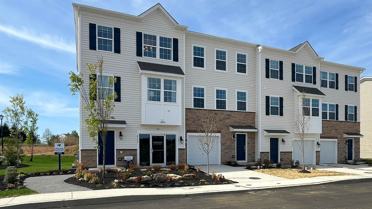 Exterior front image of the model townhome with cream horizontal panel siding and stone kneewall with white single car garage.