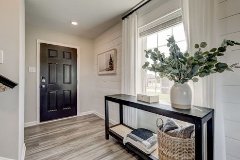 Entryway of a home with a front door opening onto a console table in front of a window with long curtains and shiplap accent trim.