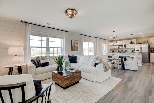 Open concept living space with a living area with plush sectional and an accent chair, dining table with seating for six, and a kitchen beyond.