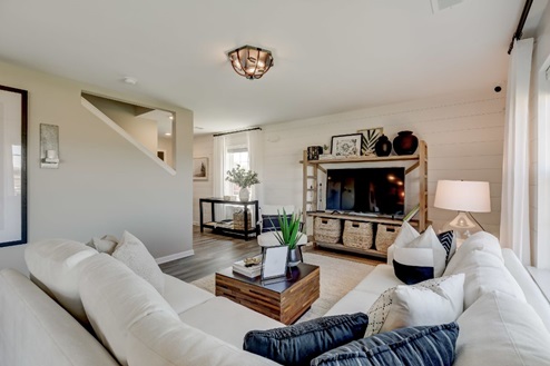 Plush sectional sofa facing an entertainment center with a coffee table between in an open-concept living room with a view of the entryway and stairs.
