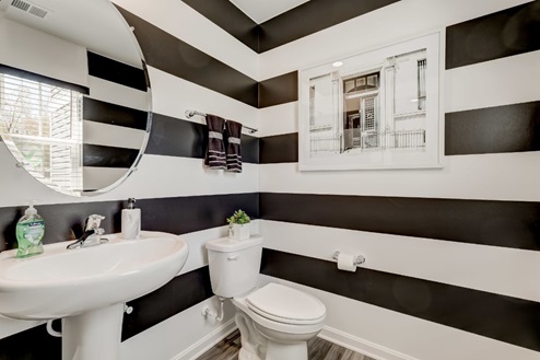Powder bathroom with bold black-and-white horizontal stripes painted on the walls, a pedestal sink, and a window for natural light.