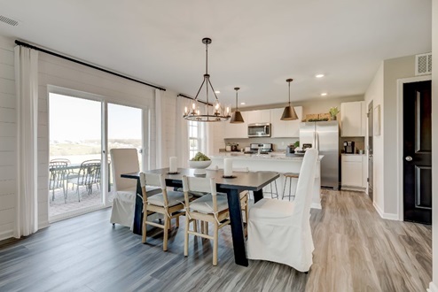 Dining area with a black wooden table surrounded by six chairs in front of sliding glass doors that provide access to the back patio.