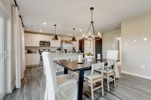 Dining area with a black wooden table surrounded by six chairs with a view into the adjoining kitchen.