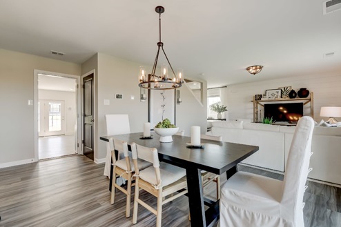 Dining area with a black wooden table surrounded by six chairs with a view into the adjoining living room and through to the garage.