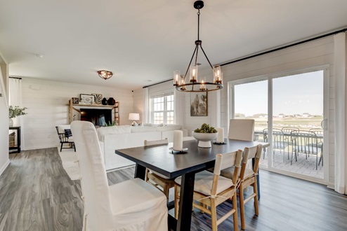 Dining area with a black wooden table surrounded by six chairs in front of sliding glass doors that provide access to the back patio.