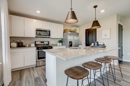 Spacious kitchen with a large center island with seating for four and an undermount sink, white, shaker-style cabinets, quartz countertops, and stainless-steel appliances.