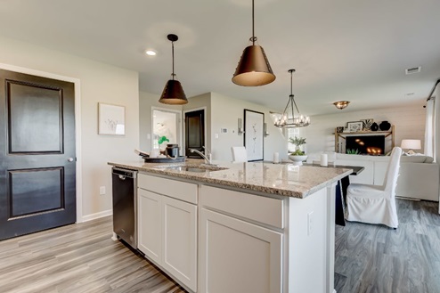 Center island in an open-concept kitchen with white, shaker-style cabinets, statement pendant lights, an undermount sink, and a stainless-steel dishwasher.