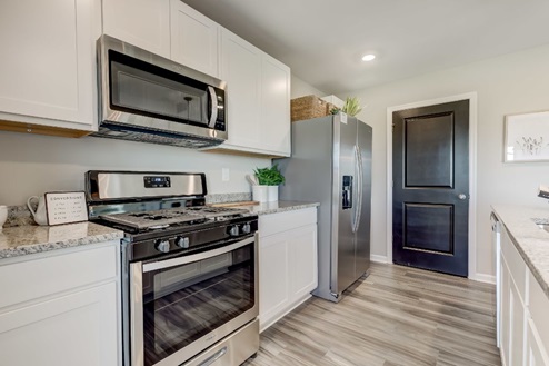 White, shaker-style cabinets and quartz countertops along the back wall of an open-concept kitchen with stainless-steel appliances.