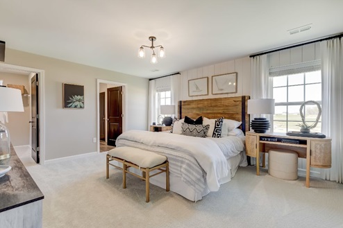 Primary bedroom with a large bed flanked by nightstands and windows with a bench at the foot and a dresser across.