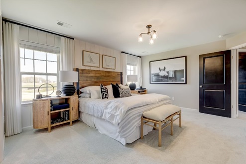 Primary bedroom with a large bed flanked by nightstands and windows with a bench at the foot.