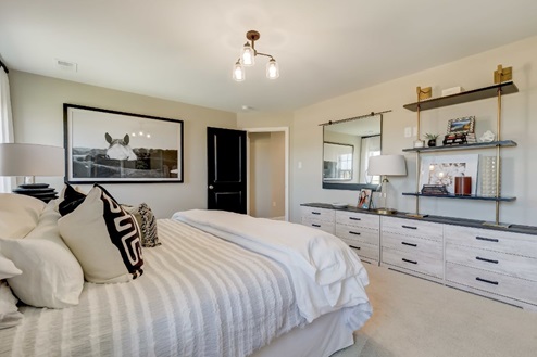 Primary bedroom with a large bed flanked by nightstands and windows with a bench at the foot and a dresser and shelving system across.