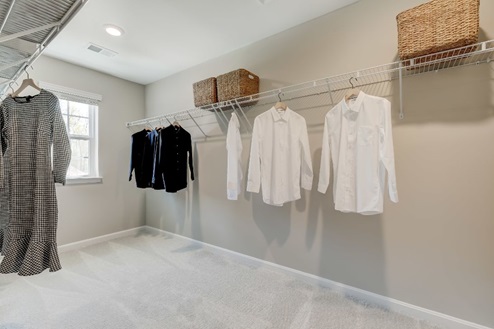 Large walk-in closet off of the primary bedroom with a window for natural lighting and two shelf-lined walls for plenty of hanging space and storage.