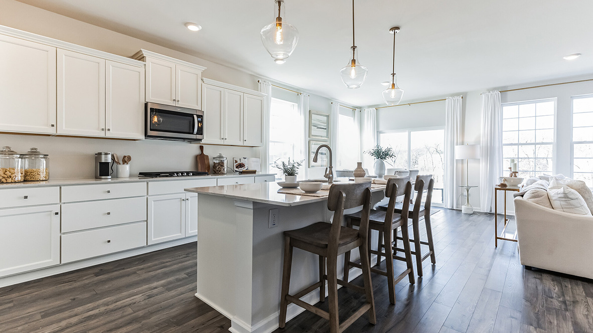 Kitchen area with stainless steel appliances, white counter tops and white cabinetry. The casual dining area behind the kitchen area but in front of the back sliding glass door.