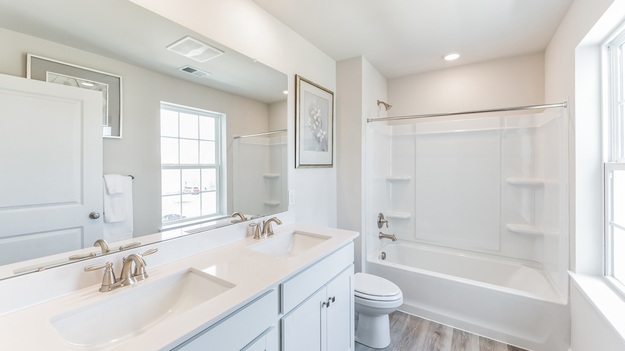A guest bathroom has a double-bowl vanity, toilet, and shower tub.