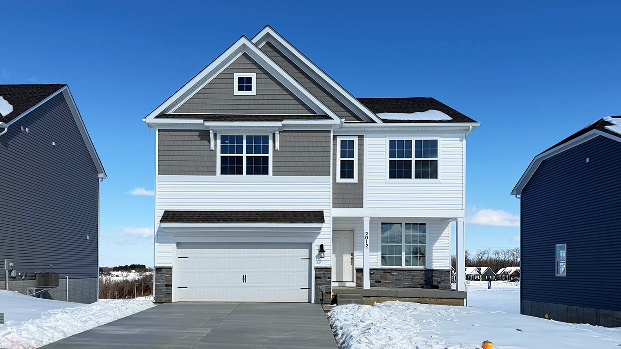 A photo of a two-story Penwell home with white siding and gray shake accent siding, stone kneewall, and a white two car garage.
