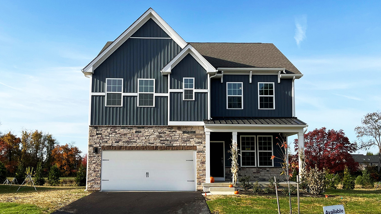 A photo of a two-story Penny home with navy board and batten siding, stone kneewall, and stone siding surrounding a white two car garage.