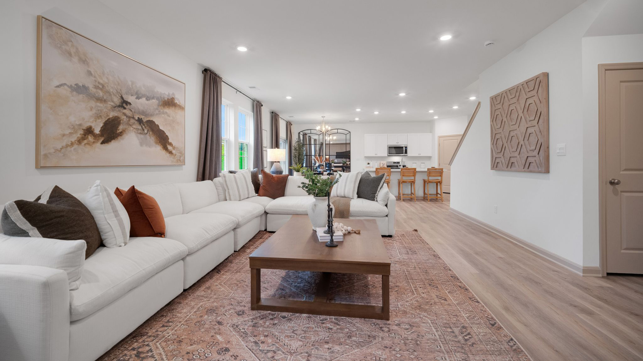 Living room with a large sectional sofa and coffee table arranged facing a wall-mounted tv above a storage console, all in front of a wall boasting three windows overlooking the back yard.