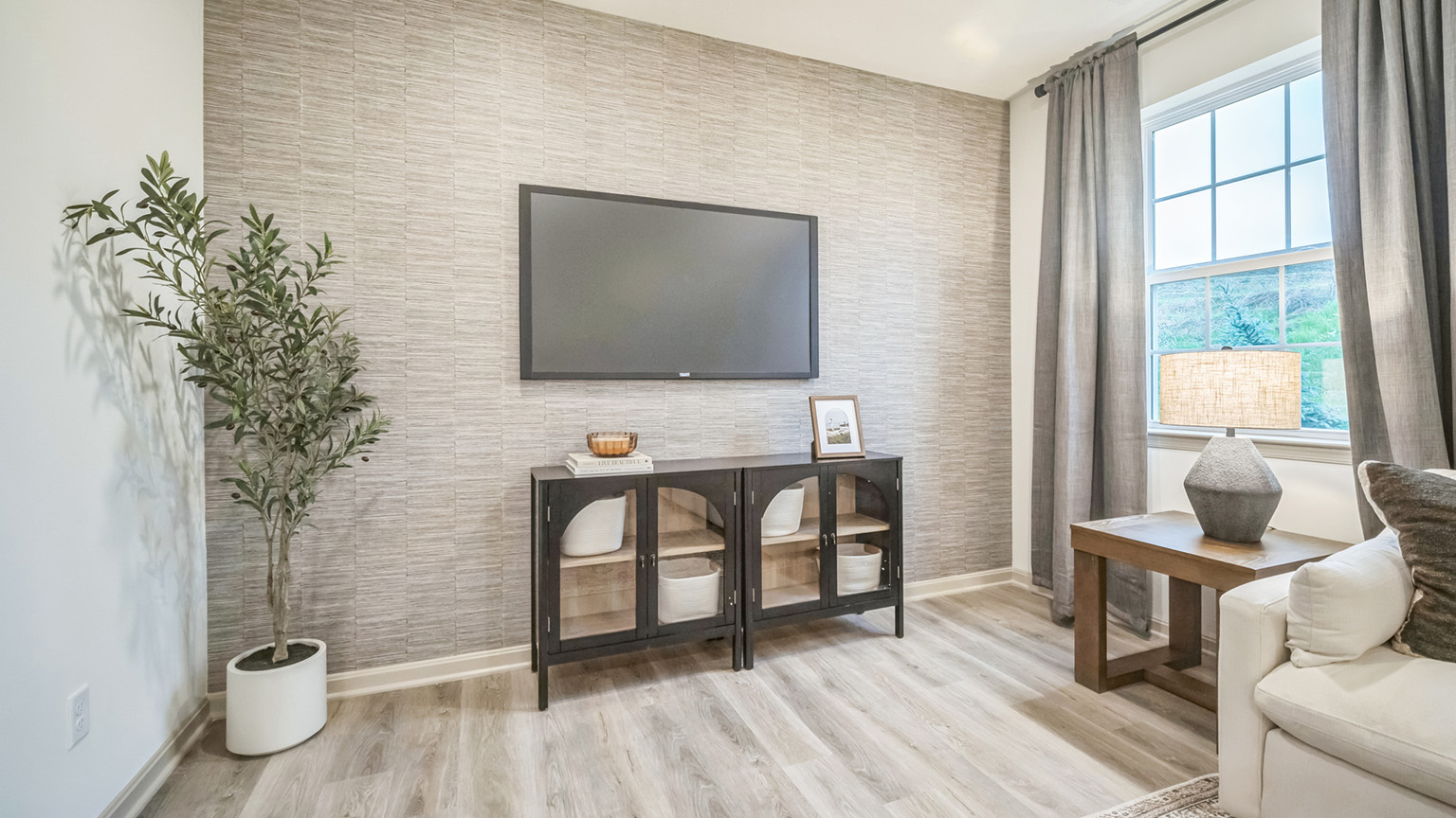 Wall-mounted tv above a storage console in front of an accent wall in an open-concept living room with a window allowing natural light to flow through.