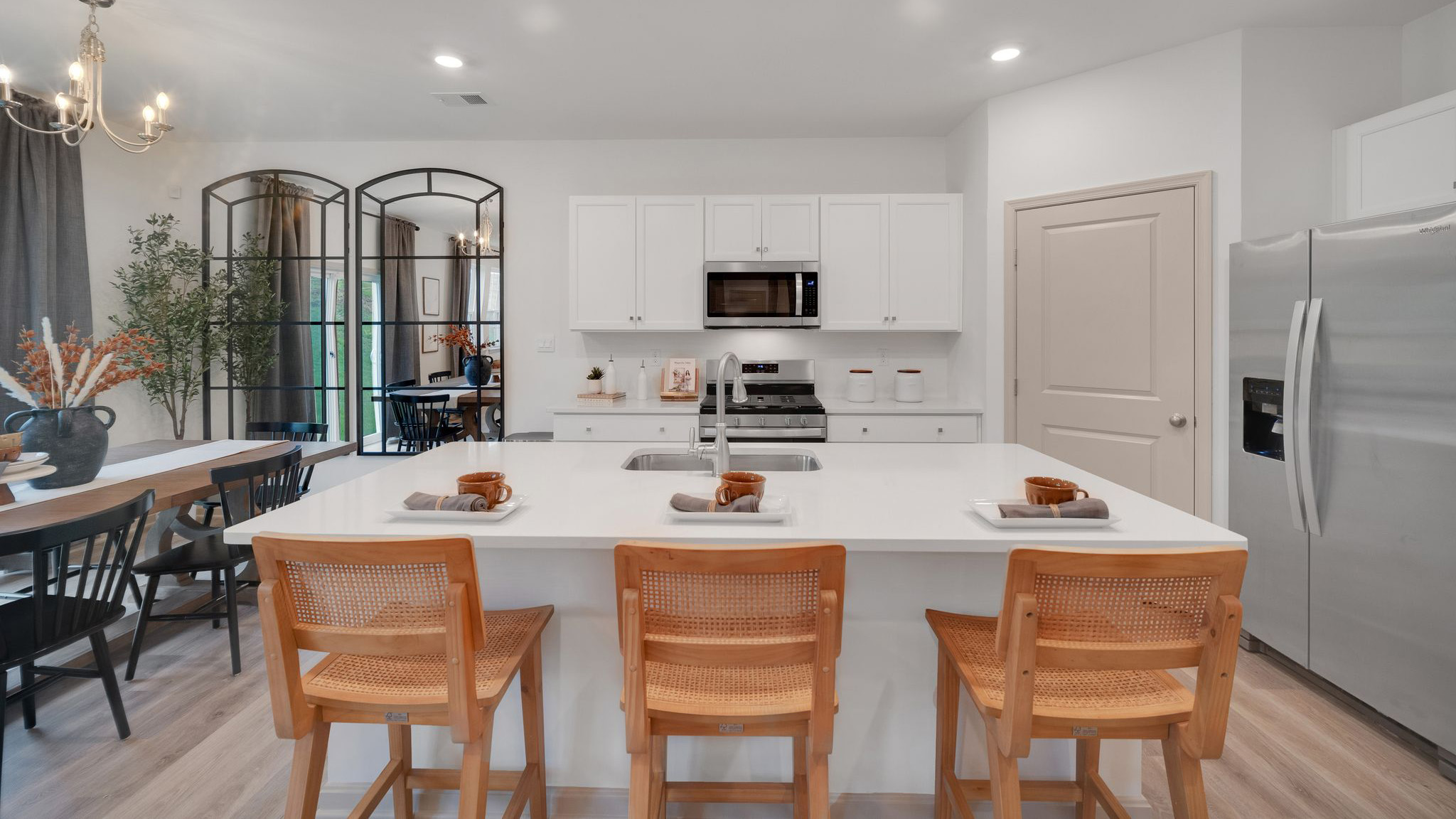 A spacious kitchen with white, shaker-style cabinets, quartz countertops, a large center island with undermount sink and seating for three, and a stainless-steel appliance package.