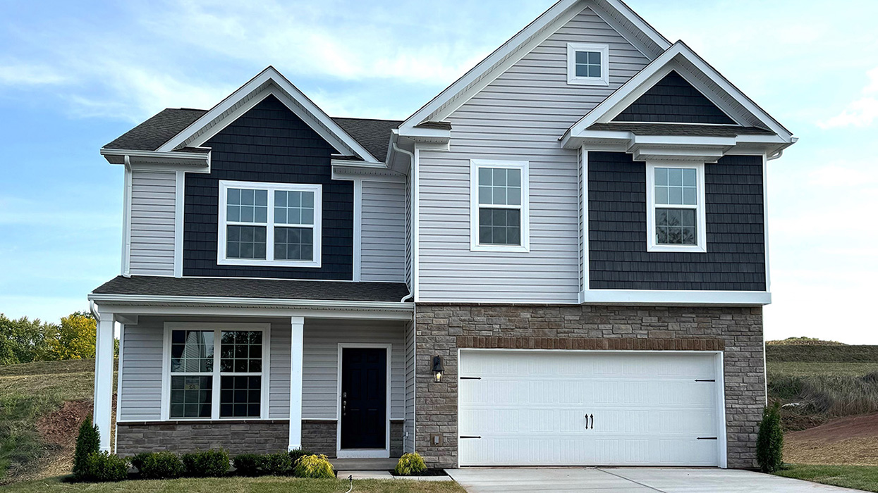 A photo of a two-story Henley home with misty blue and gray siding, stone kneewall, brown front door, and stone siding surrounding a white two car garage.