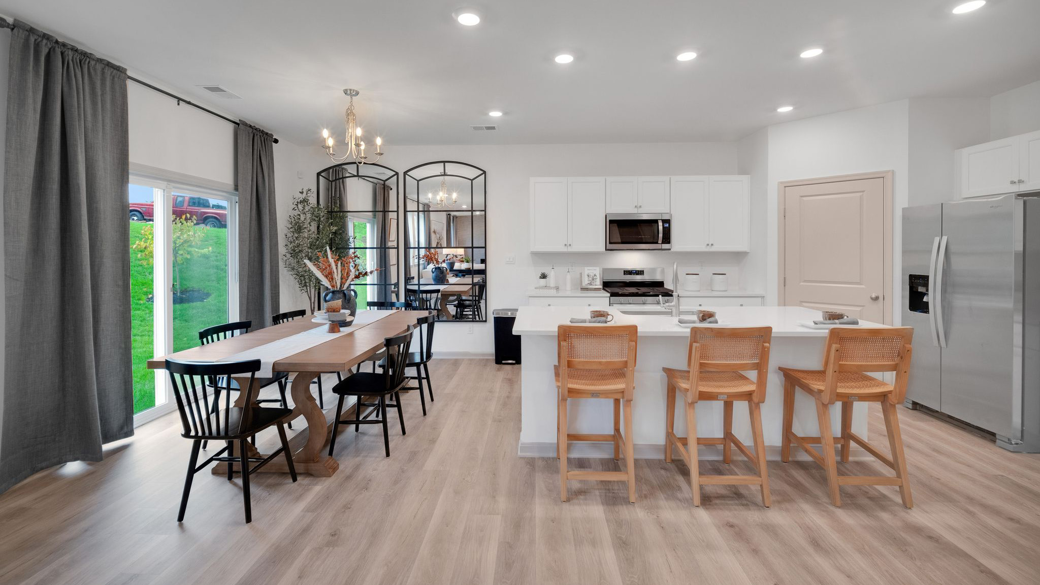 A spacious kitchen with white, shaker-style cabinets, quartz countertops, a large center island with undermount sink and seating for three, and a stainless-steel appliance package that flows into an adjoining dining area that boasts a wooden table surrounded by six chairs.