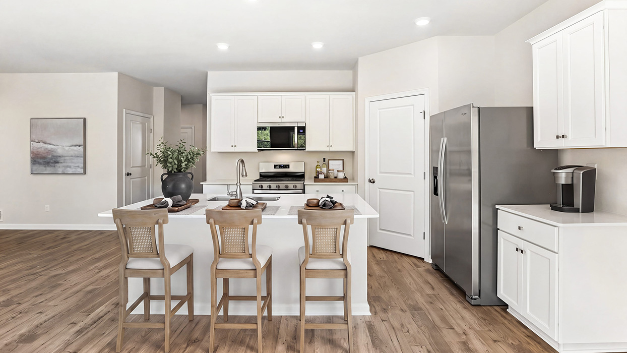 Kitchen with large island, white shaker cabinets, stainless steel refrigerator, and convenient pantry storage door.