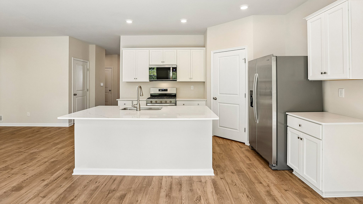 Kitchen with large island, white shaker cabinets, stainless steel refrigerator, and convenient pantry storage door.
