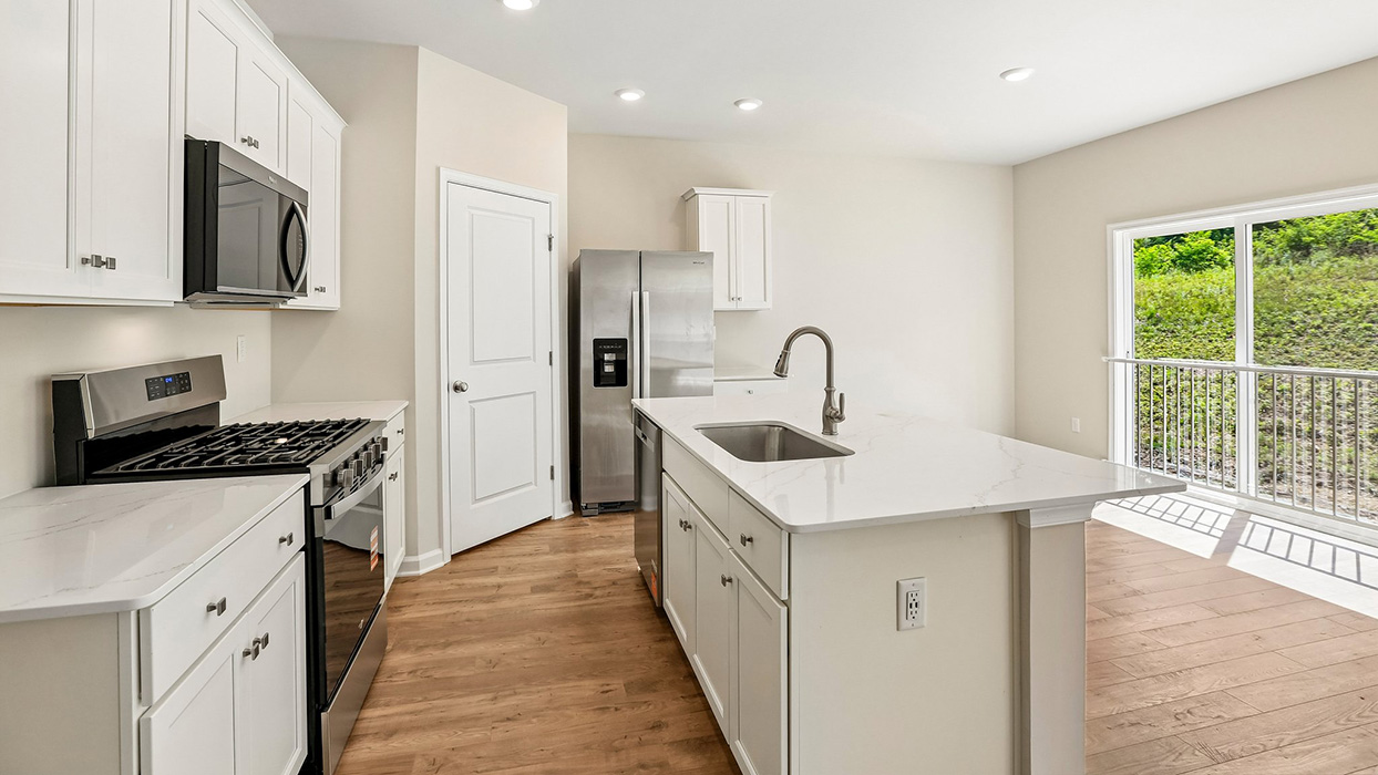 Kitchen view with island seating potential, stainless steel appliances, and open sightlines into the living area.