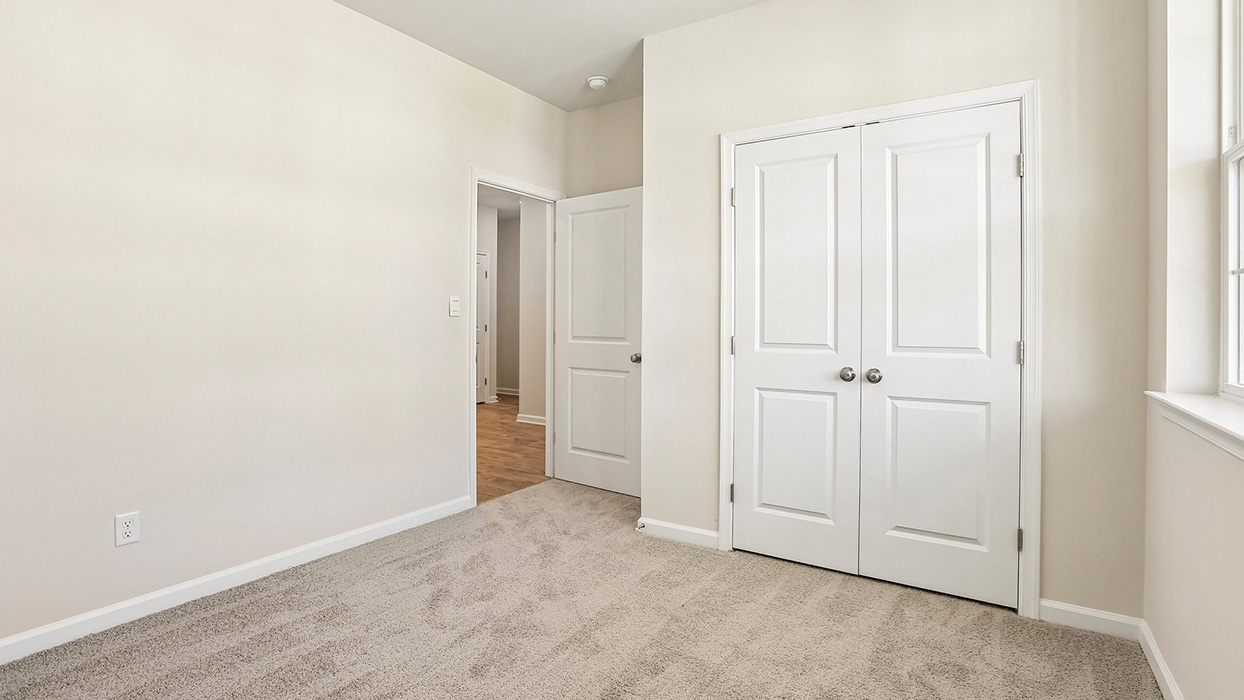 Bedroom with plush carpet, double-door closet, and neutral walls with natural light from nearby window.