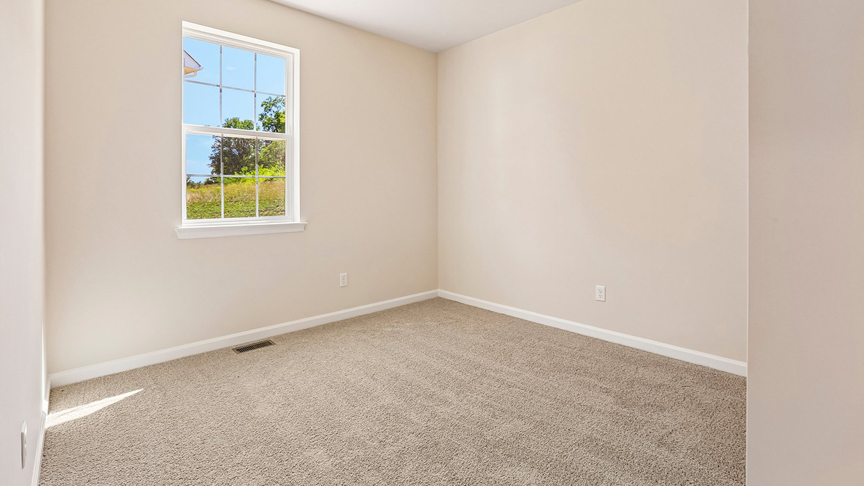 Secondary bedroom with soft carpeting, neutral tones, and window providing natural backyard views.