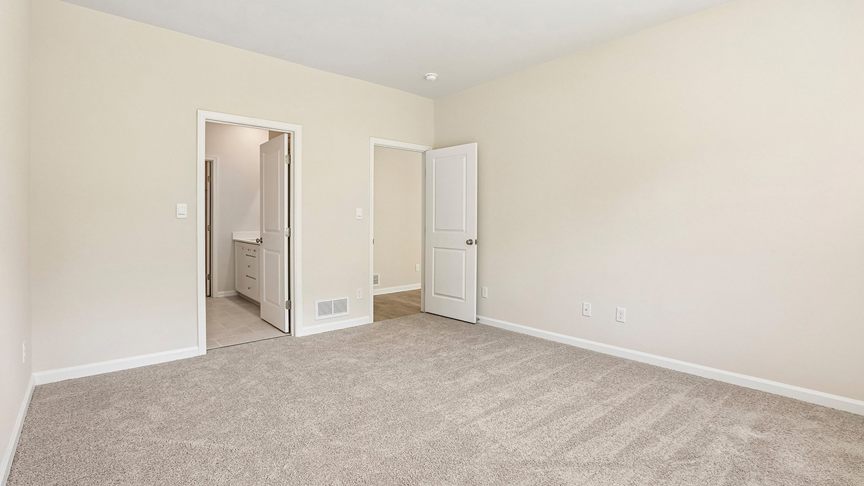 Primary bedroom showing entry to en-suite bath and closet with neutral finishes and carpet flooring.