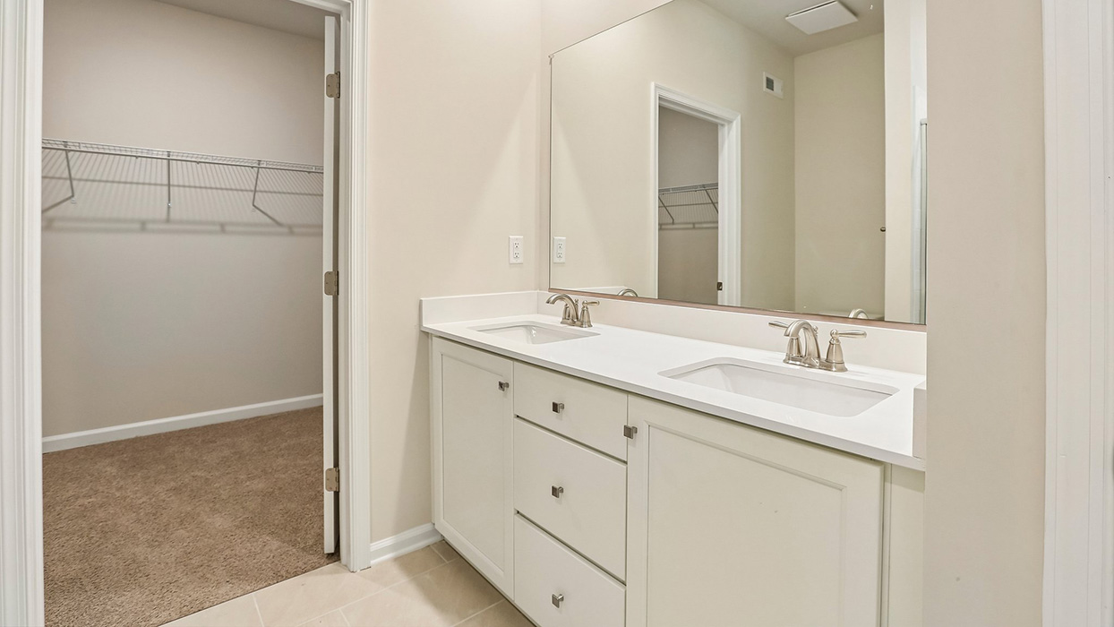 Primary bathroom with dual-sink vanity, large mirror, and adjacent walk-in closet access.