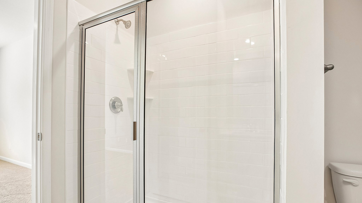 Walk-in shower with glass doors, white tile surround, and built-in shelving niche.