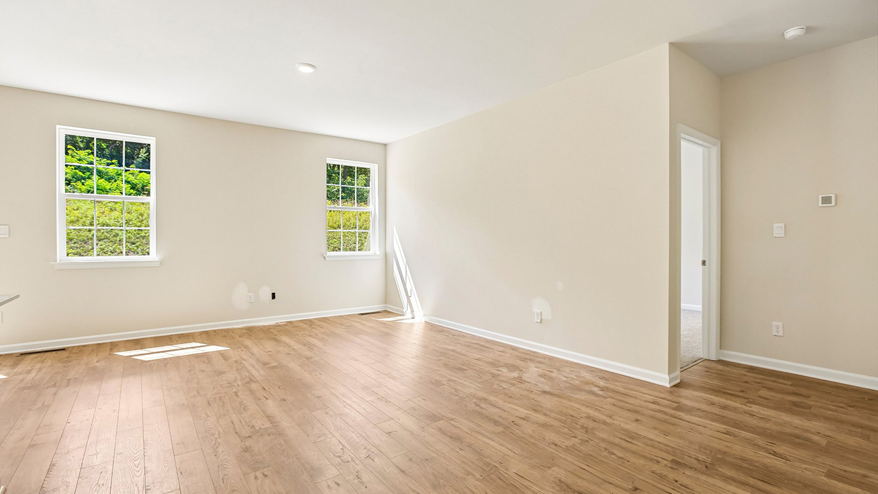 Open living area with wood flooring, large windows for natural light, and staircase access tucked along the wall.