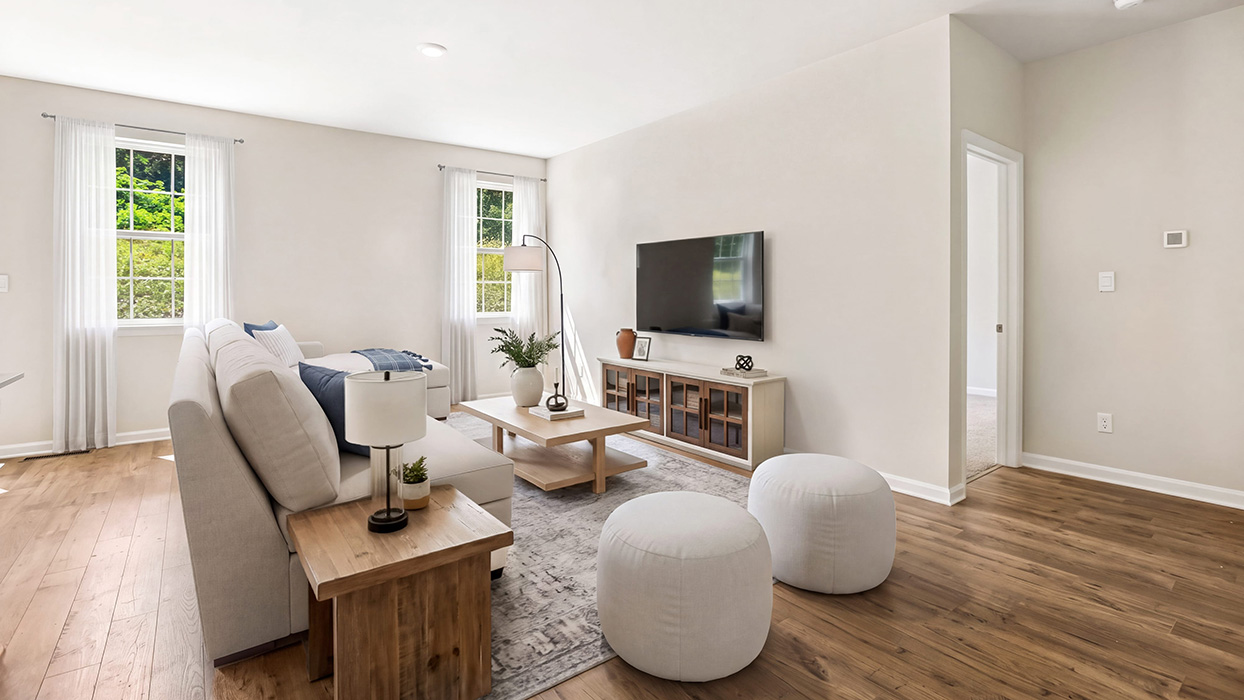 Open living area with wood flooring, large windows for natural light, and staircase access tucked along the wall.