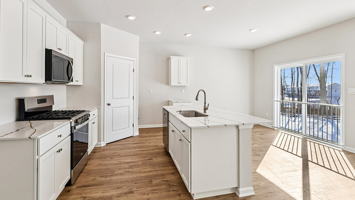 A wide angle view of the kitchen, white kitchen cabinets, stanless steel appliances, and large island with pantry in the back left corner