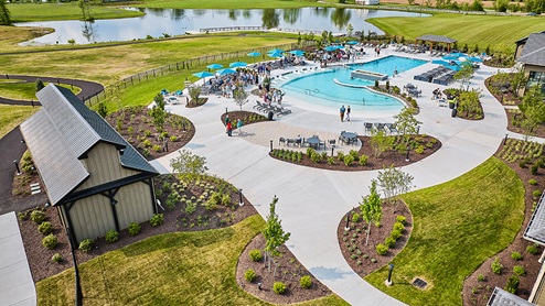 Drone photo of Amblebrook's amenity area that includes a large pool, plenty of seating, inviting landscaping, and a pond with pier beyond the pool fence.