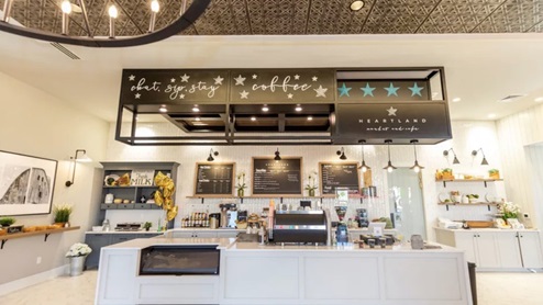 Coffee bar with a large island counter, storage cabinets on the back wall, chalk-board menus, and various coffee equipment and ingredients.