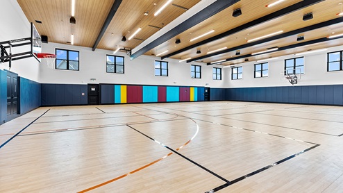 Indoor basketball court with padded walls, wood-plank ceiling, and high windows to allow lots of natural light.