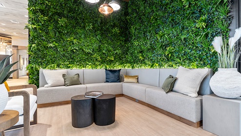 Accent wall adorned with faux foliage behind a built-in bench seat that anchors a seating area featuring a coffee table, accent chairs, and end tables.