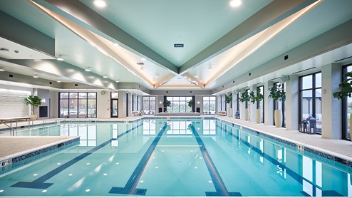 Indoor pool with lanes for swimming laps and walls of windows overlooking other outdoor amenities.