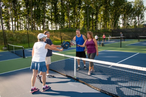 Two couples greeting each other over the net on a pickleball court.