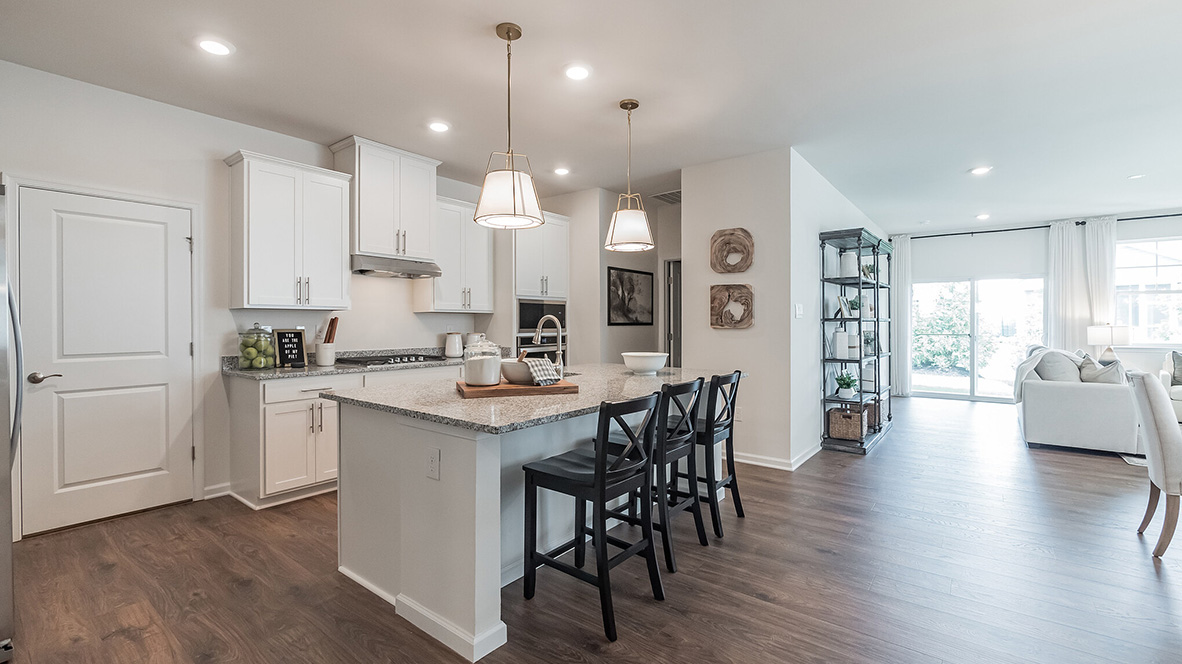A view into the kitchen area and eat-in island and a view to the pantry closet and connecting laundry closet.