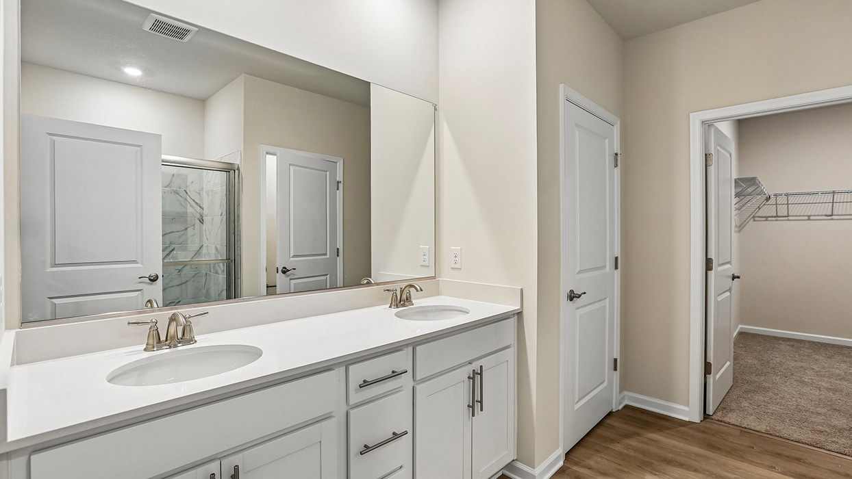 Primary bathroom featuring a dual-sink vanity, walk-in closet access, and a functional layout designed to streamline daily routines.