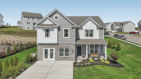 Two-story home with a covered front porch, horizontal plank siding in complimentary colors of taupe and cream with a stone water-table accent, and a sales center front on the two-car garage.