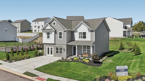 Two-story home with a covered front porch, horizontal plank siding in complimentary colors of taupe and cream with a stone water-table accent, and a sales center front on the two-car garage.