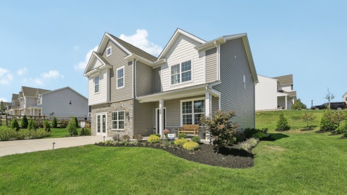 Two-story home with a covered front porch, horizontal plank siding in complimentary colors of taupe and cream with a stone water-table accent, and a sales center front on the two-car garage.